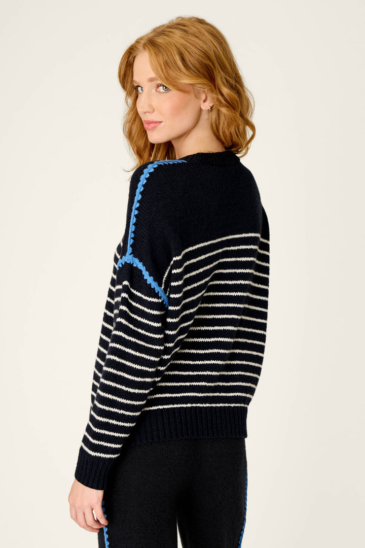 A woman with wavy red hair wears the P.J. Salvage C'est La Vie Merci Sweater—a black and white striped knit with blue accents—posing slightly turned to the side against a light background.