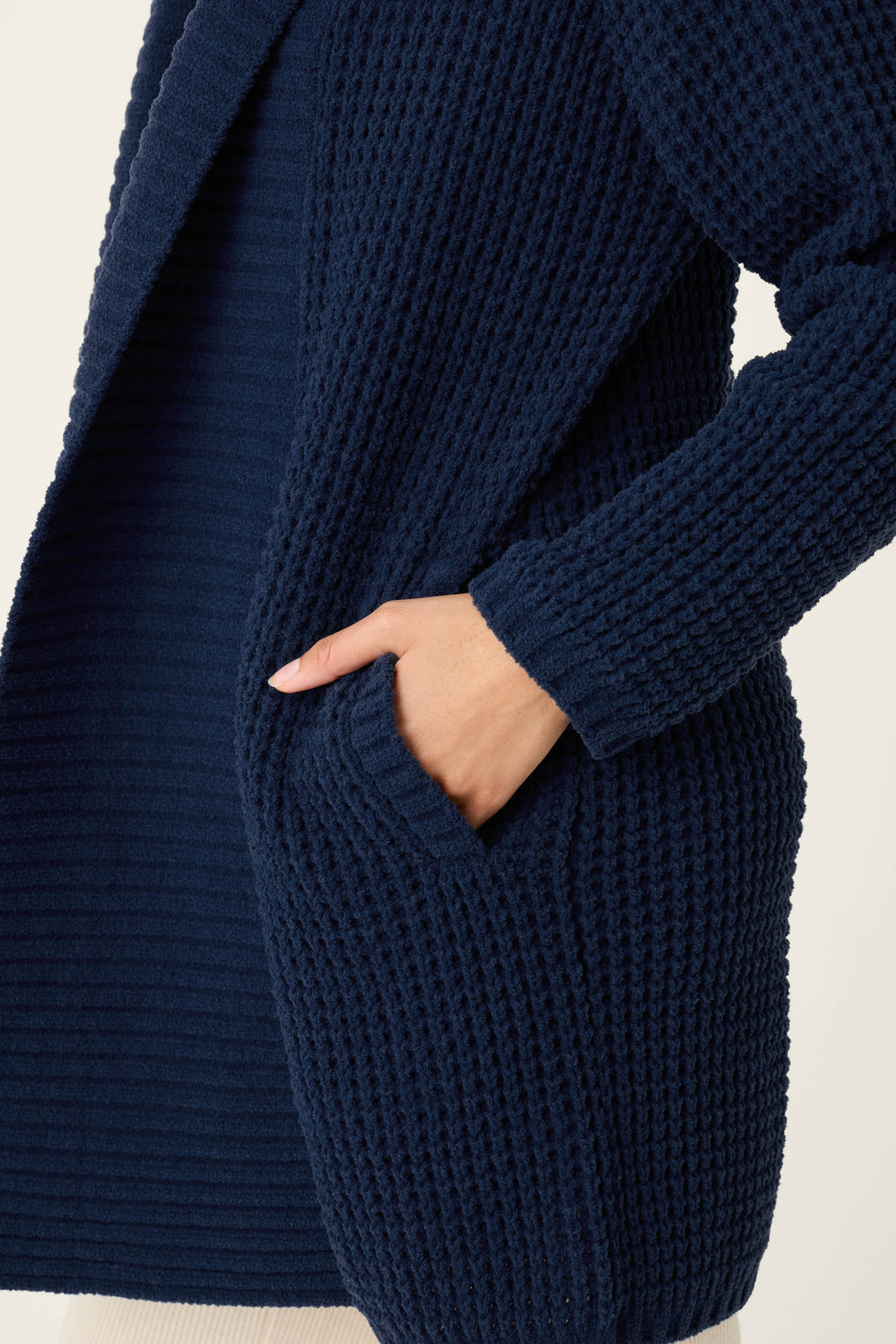 A person is shown from the torso up against a plain light background, wearing the P.J. Salvage Cozy Chenille Waffle Deep Navy Cardigan with their right hand tucked into a pocket.
