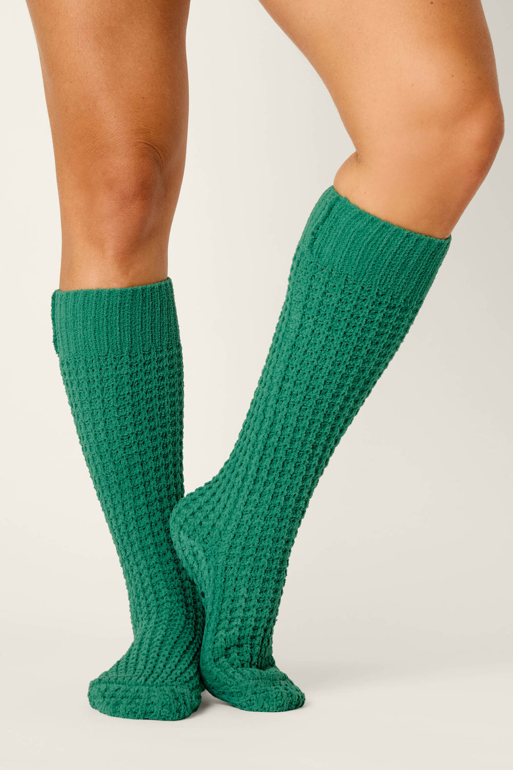 A person wearing Cozy Chenille Waffle Green Mid-Calf Socks by P.J. Salvage stands with legs crossed at the ankles against a plain light background.