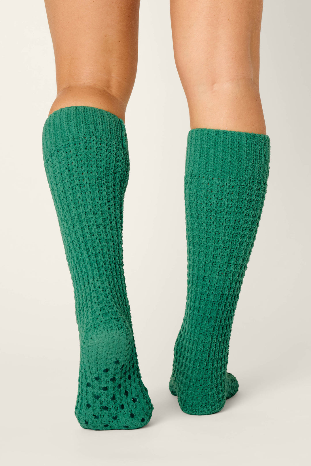 A person wearing P.J. Salvage’s Cozy Chenille Waffle Green Mid-Calf Socks stands with their back to the camera against a plain, light background.