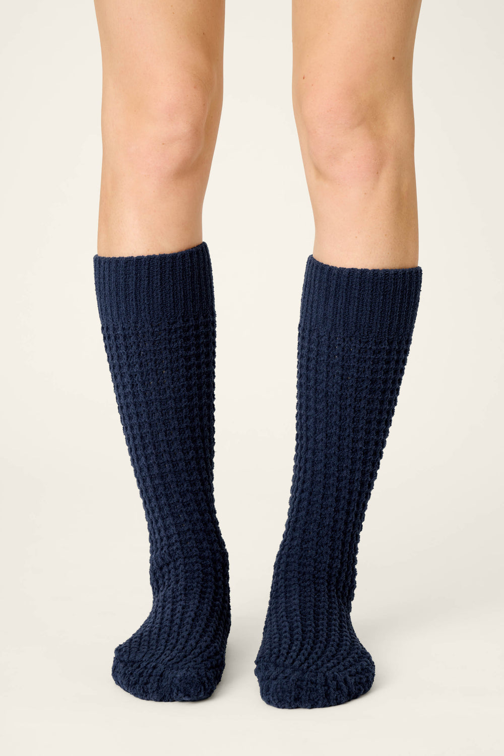 A person wears P.J. Salvage Cozy Chenille Waffle Deep Navy Mid-Calf Socks, standing on a light, neutral background with only their legs and feet visible, facing forward.