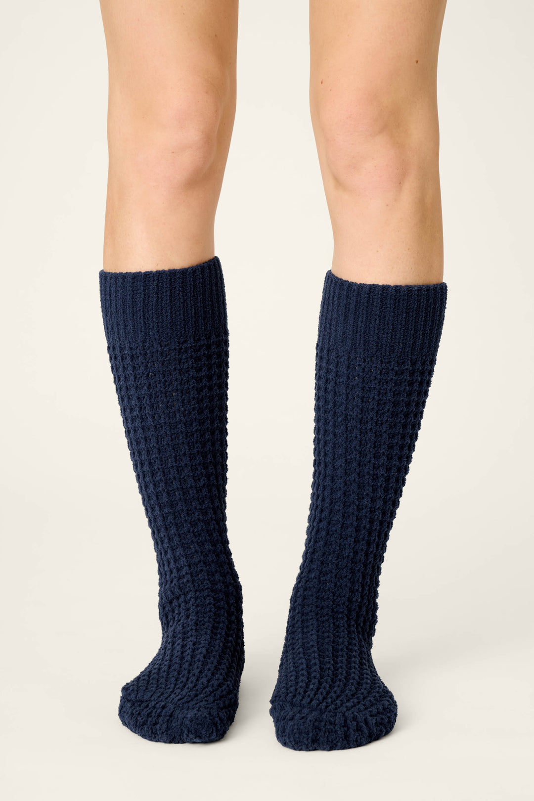 A person wears P.J. Salvage Cozy Chenille Waffle Deep Navy Mid-Calf Socks, standing on a light, neutral background with only their legs and feet visible, facing forward.