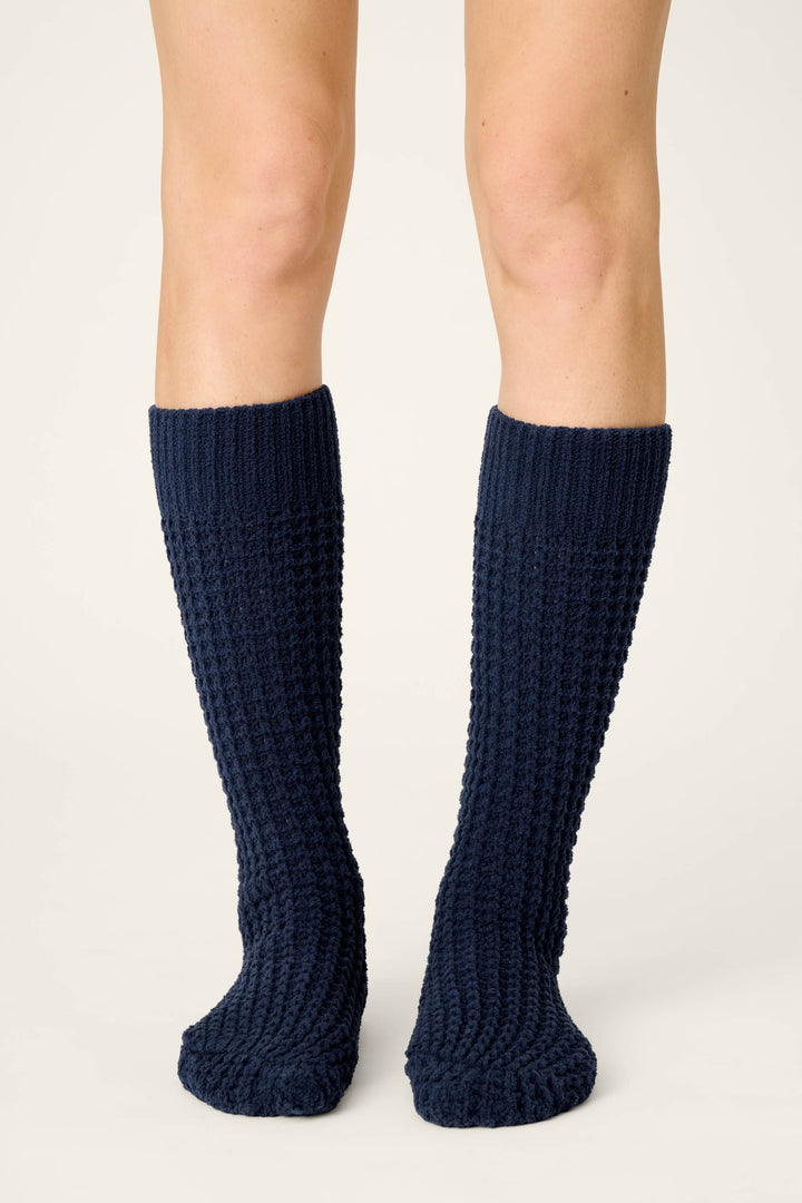 A person wears P.J. Salvage Cozy Chenille Waffle Deep Navy Mid-Calf Socks, standing on a light, neutral background with only their legs and feet visible, facing forward.