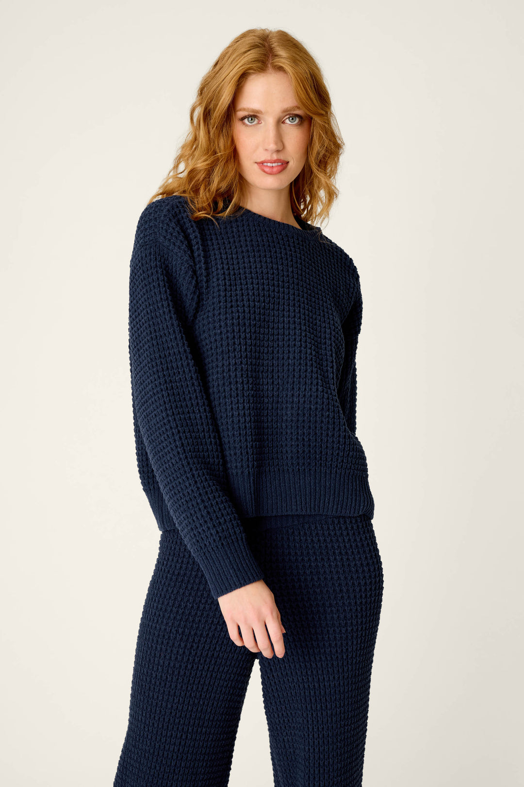 A woman with wavy red hair wears the P.J. Salvage Cozy Chenille Waffle Deep Navy Sweater, paired with matching pants, standing against a plain light background.