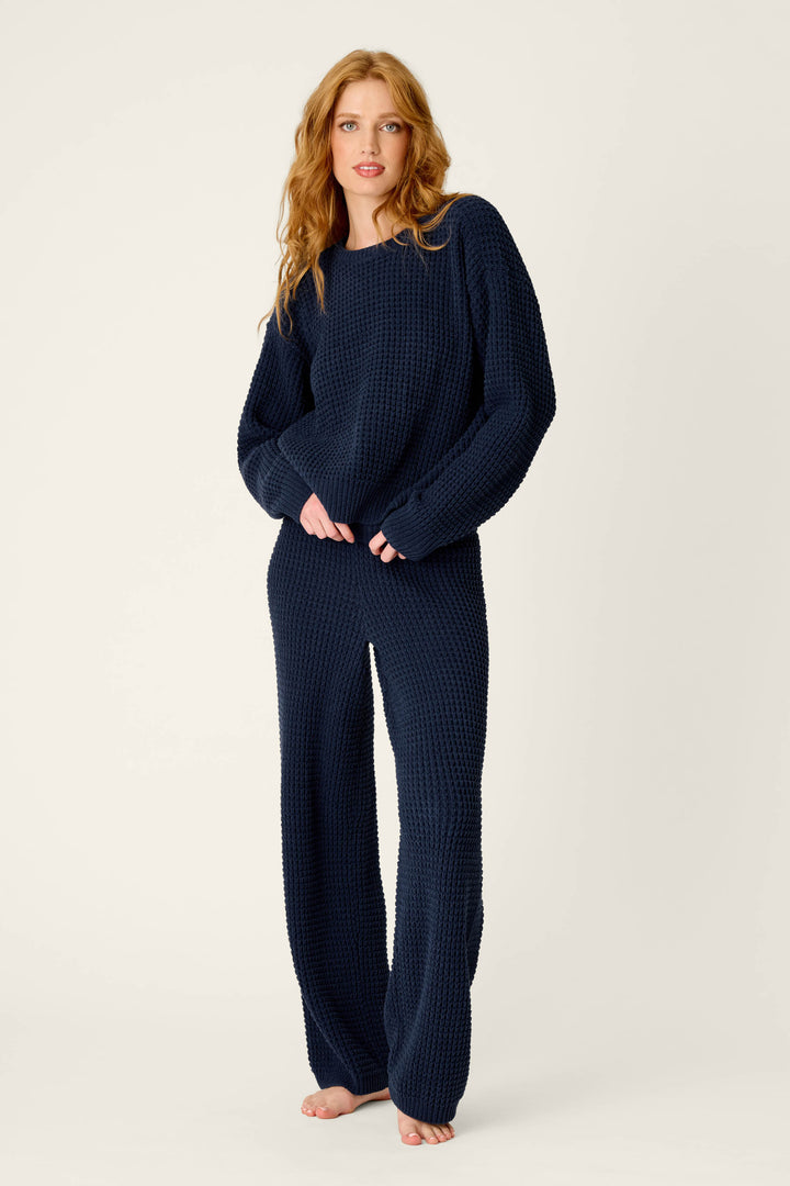 A person with long, wavy hair wears the P.J. Salvage Cozy Chenille Waffle Deep Navy Sweater with matching pants, standing barefoot against a light background.