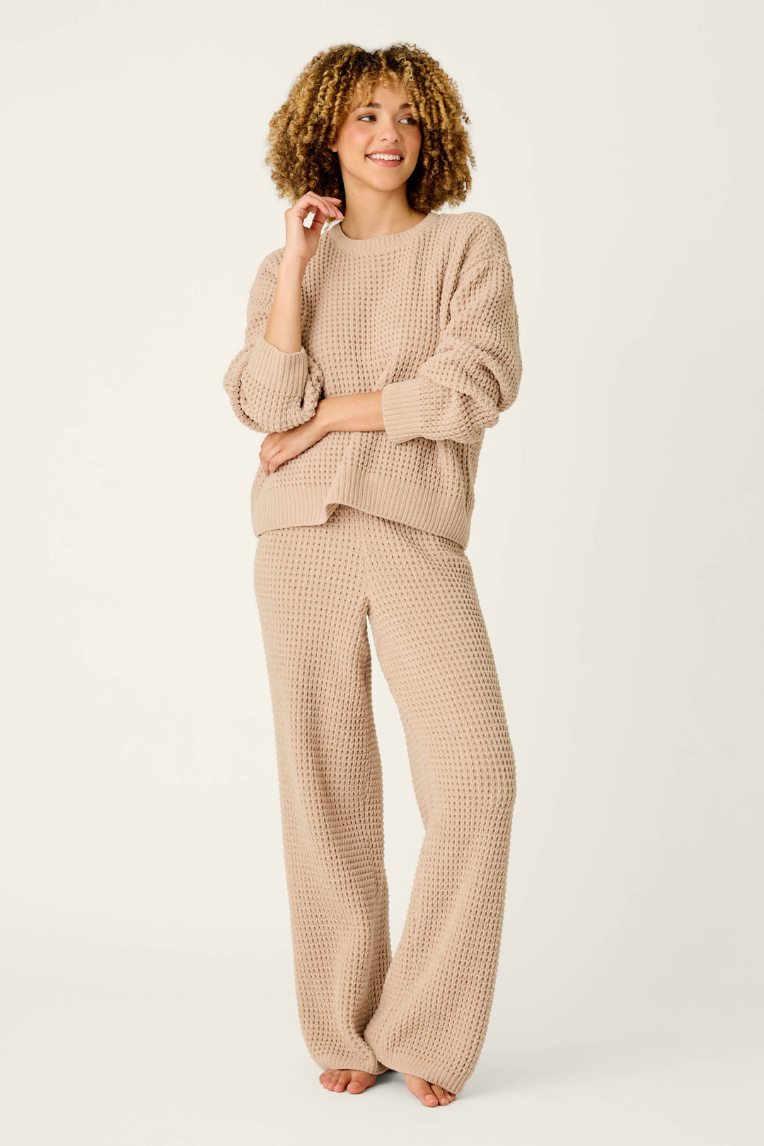Wearing the P.J. Salvage Cozy Chenille Waffle Smoky Beige Sweater, a person with curly hair stands barefoot and smiling against a plain light background, paired with matching wide-leg pants.