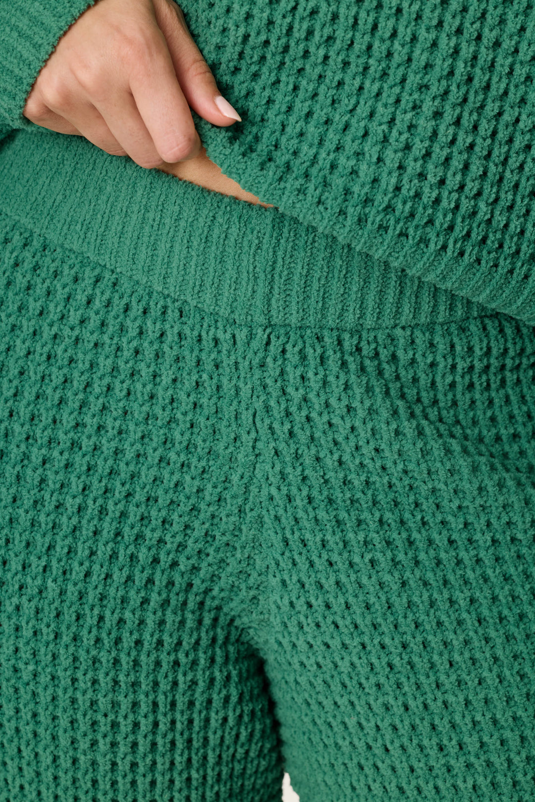 Close-up of a person wearing P.J. Salvage Cozy Chenille Waffle Green Lounge Pants, paired with a matching textured waffle-knit sweater. One hand gently lifts the sweater to reveal the pants’ waistband.