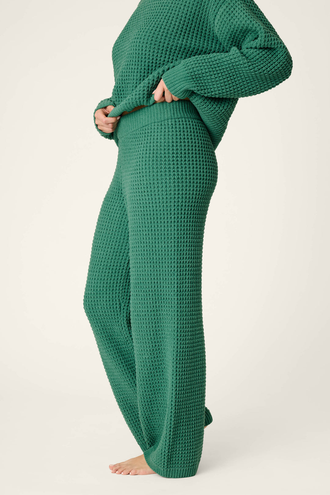 A person wearing the P.J. Salvage Cozy Chenille Waffle Green Lounge Pants, paired with a matching green waffle-knit long-sleeve top, standing barefoot against a plain background.
