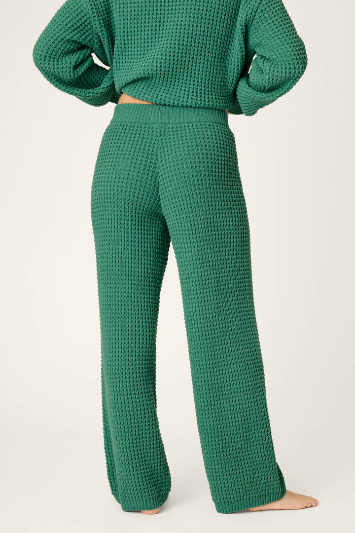 A person standing barefoot, shown from the back against a plain, light background, wears P.J. Salvage Cozy Chenille Waffle Green Lounge Pants paired with a matching textured green knit sweater.