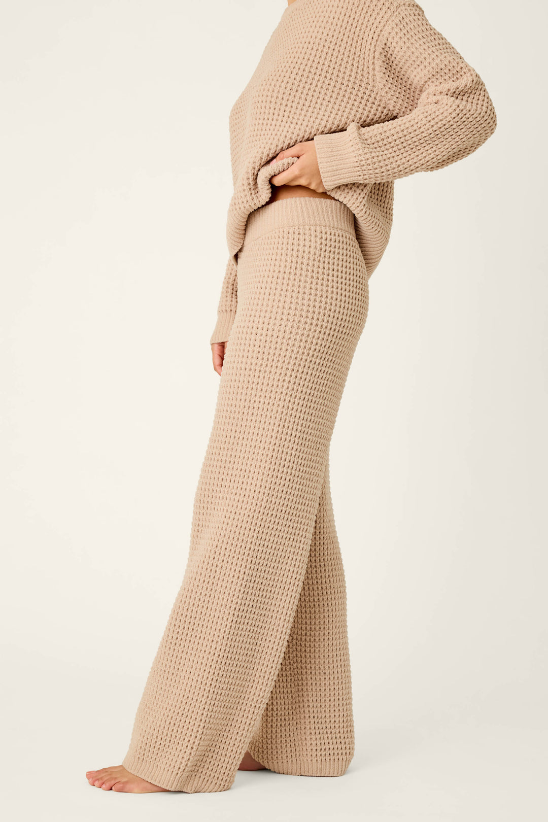 A person is shown from mid-face down, barefoot against a plain white background, wearing P.J. Salvage Cozy Chenille Waffle Smoky Beige Lounge Pants and a coordinating textured knit sweater.