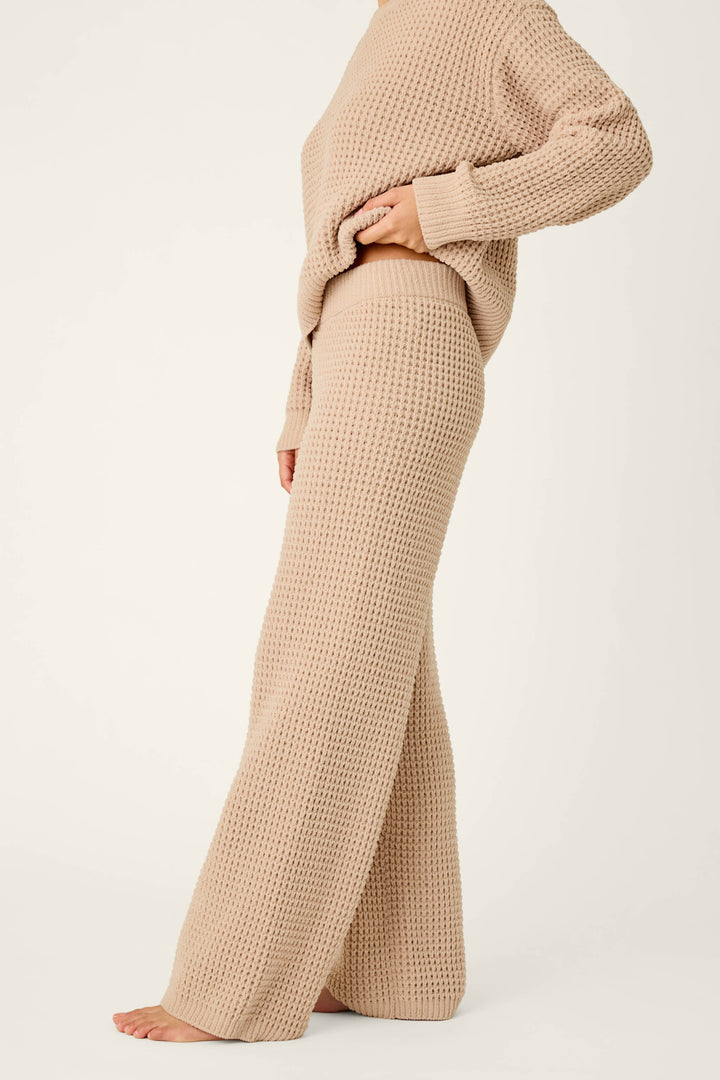 A person is shown from mid-face down, barefoot against a plain white background, wearing P.J. Salvage Cozy Chenille Waffle Smoky Beige Lounge Pants and a coordinating textured knit sweater.