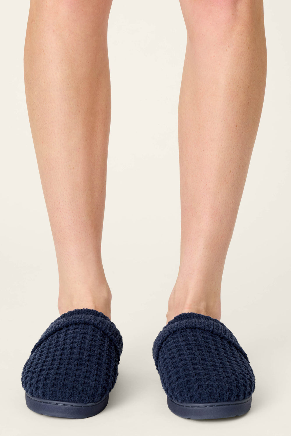 A person wearing P.J. Salvage Cozy Chenille Waffle Deep Navy Slippers stands on a light floor, visible from the knees down.