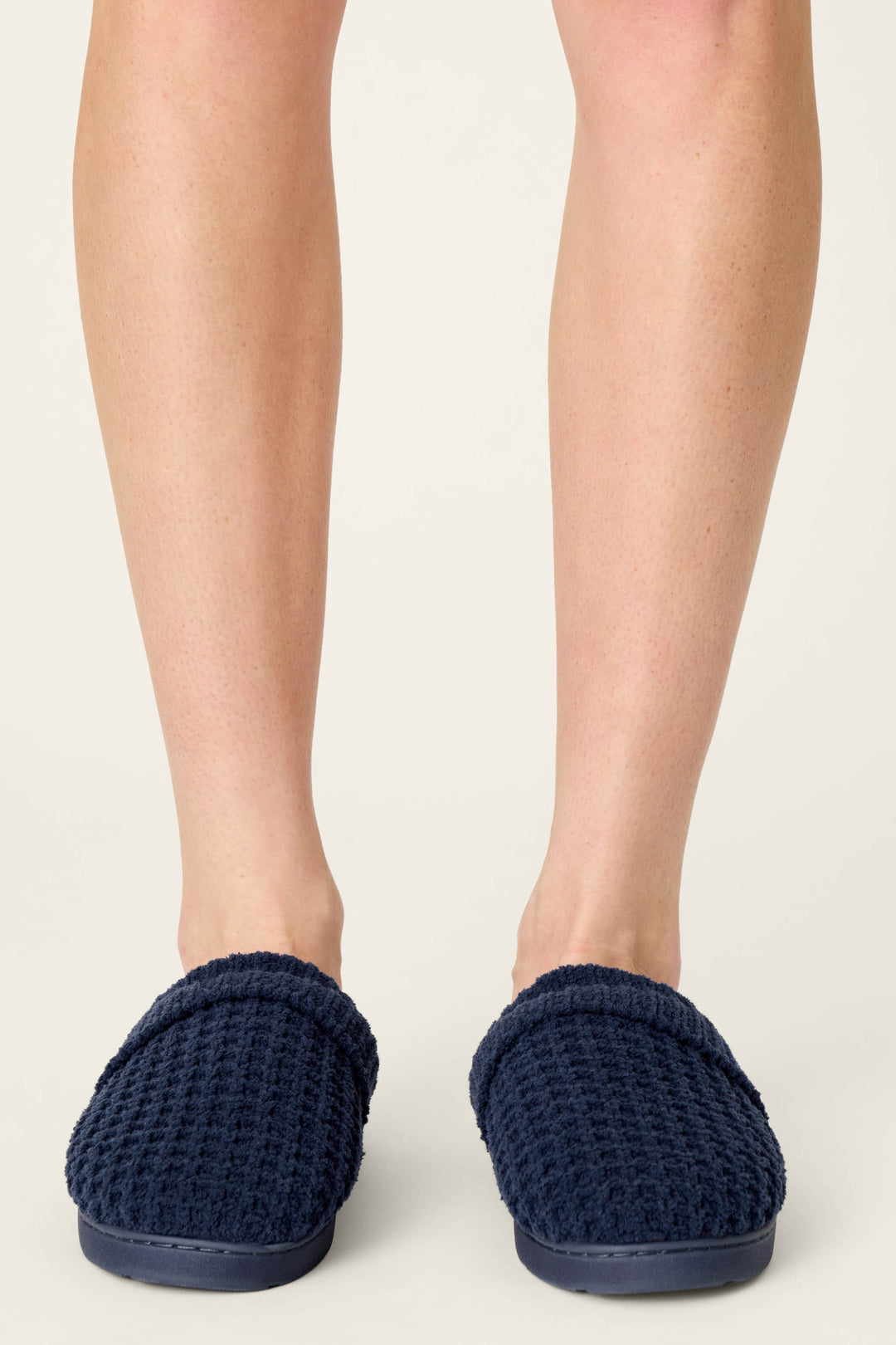 A person wearing P.J. Salvage Cozy Chenille Waffle Deep Navy Slippers stands on a light floor, visible from the knees down.