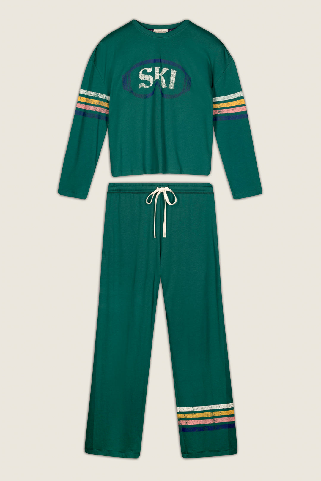 The P.J. Salvage Ski Goggles Graphic Long Sleeve Pajama Set is a green two-piece loungewear set featuring a long-sleeve top with “SKI” lettering and striped accents on the sleeves, while the matching drawstring pants have coordinating stripes near the cuffs. Both pieces are finished with yellow, white, and purple accents for a stylish touch.