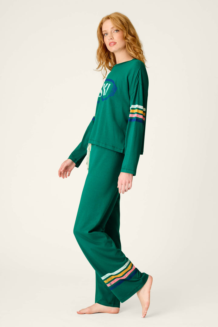 A woman with long blonde hair is wearing the P.J. Salvage Ski Goggles Graphic Long Sleeve Pajama Set, which features multicolored stripes on the sleeves and pant legs, as she stands barefoot against a plain background.