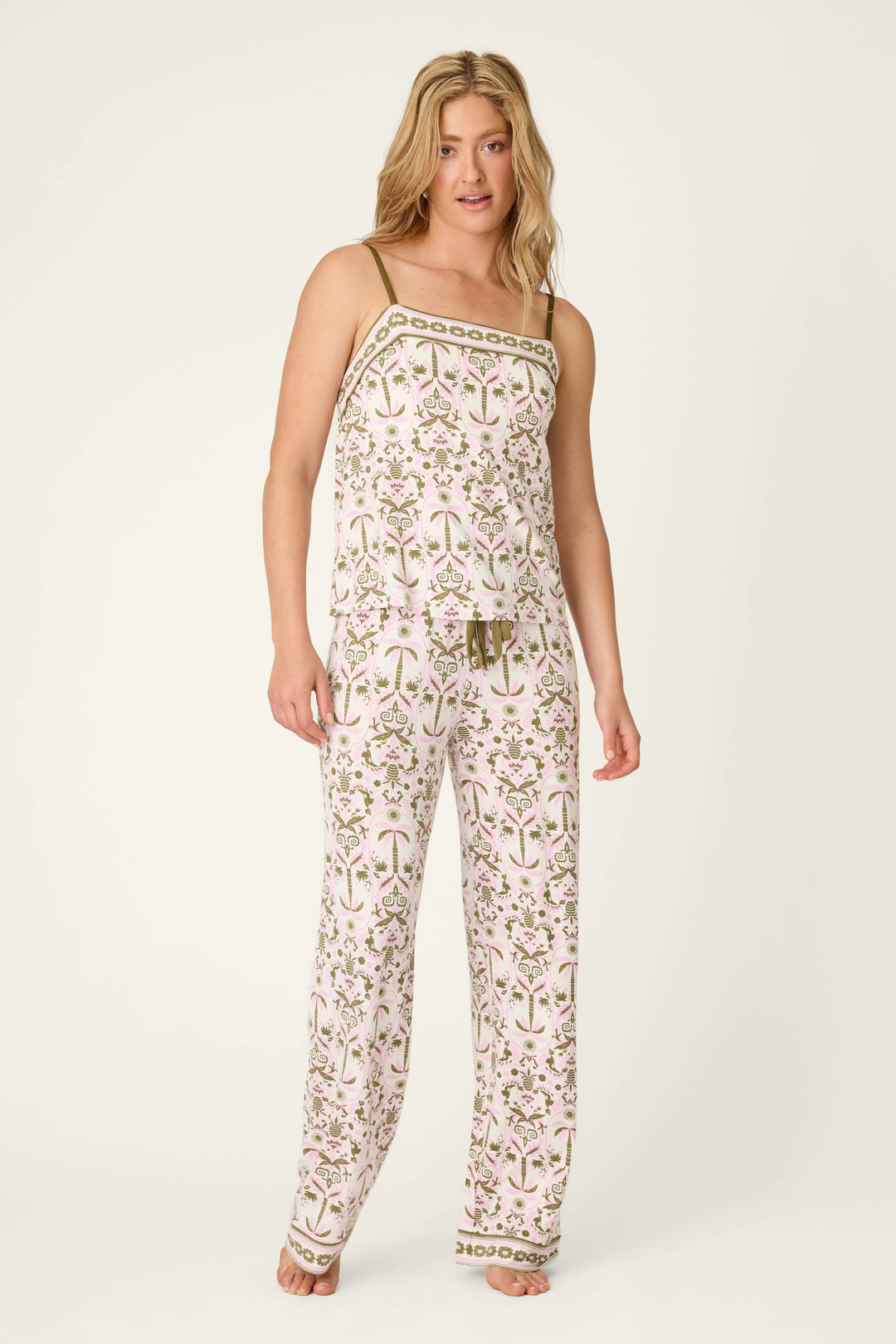 A person stands barefoot in the Déjà Vu Dreams Tiki Time Long PJ Set by P.J. Salvage, featuring a matching botanical print in pink and green on white, with a sleeveless, thin-strap top and loose-fitting pants.