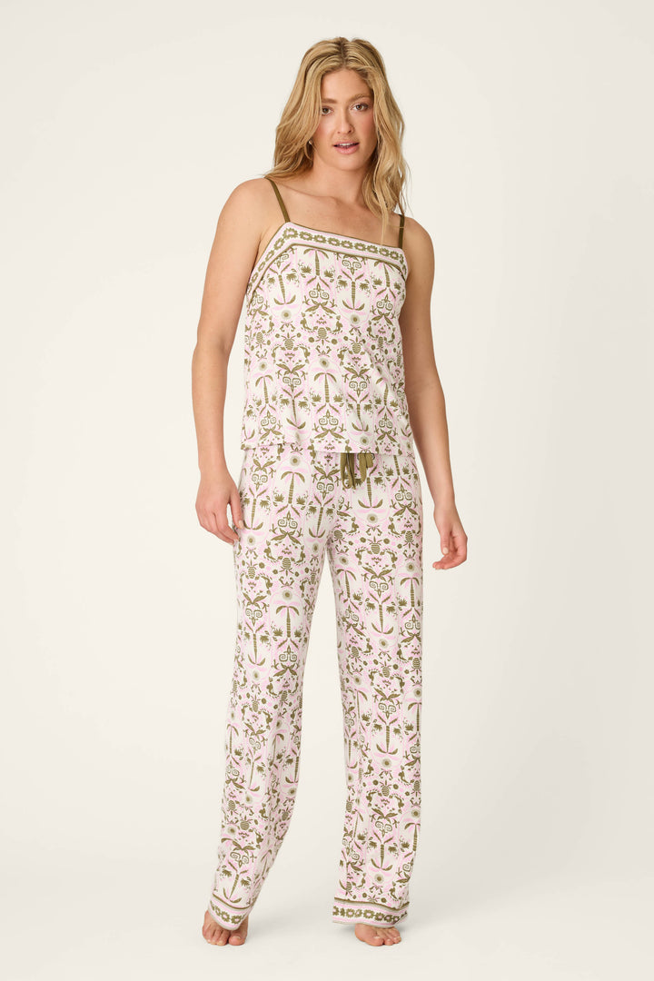 A person stands barefoot in the Déjà Vu Dreams Tiki Time Long PJ Set by P.J. Salvage, featuring a matching botanical print in pink and green on white, with a sleeveless, thin-strap top and loose-fitting pants.