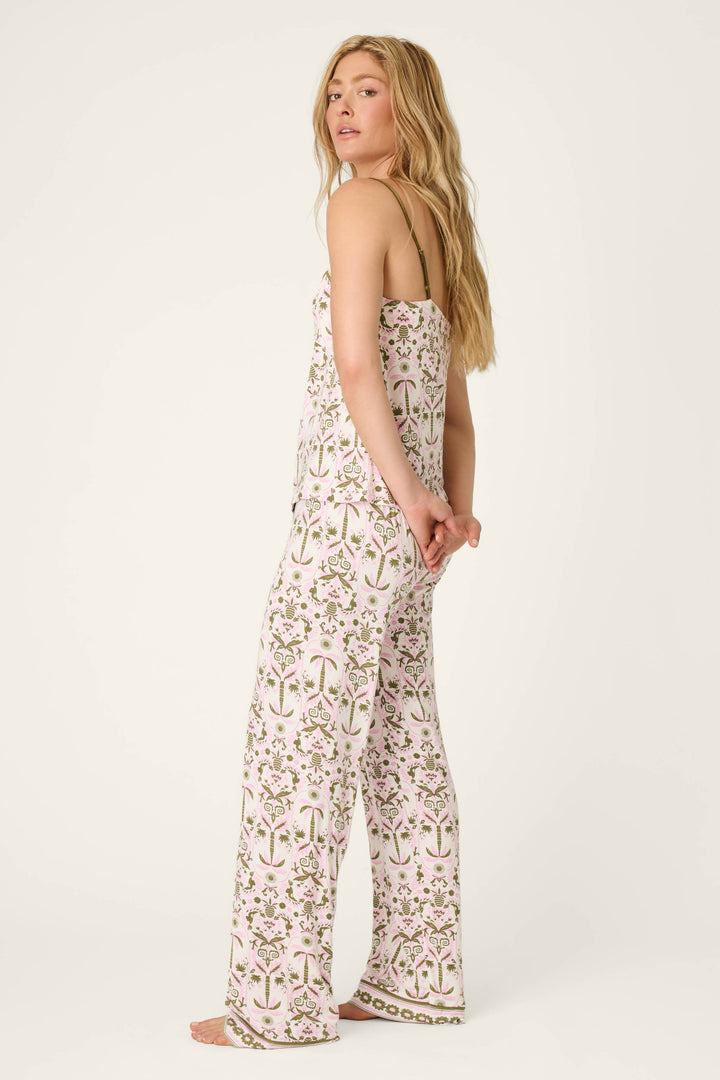 A person with long blonde hair stands barefoot, looking over their shoulder, wearing the Déjà Vu Dreams Tiki Time Long PJ Set by P.J. Salvage—a matching sleeveless top and wide-leg pants with a pink and green floral print on white.