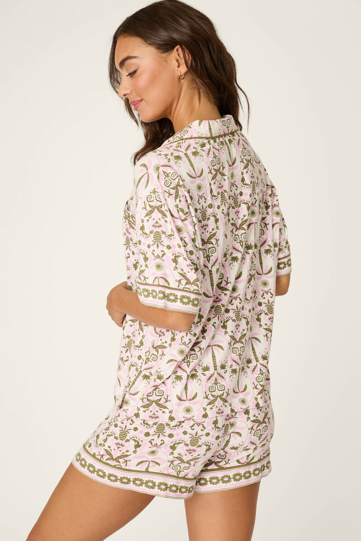 Woman with long brown hair, facing sideways and looking down, wears the P.J. Salvage Déjà Vu Dreams Tiki Time Short Sleeve Top against a neutral background.
