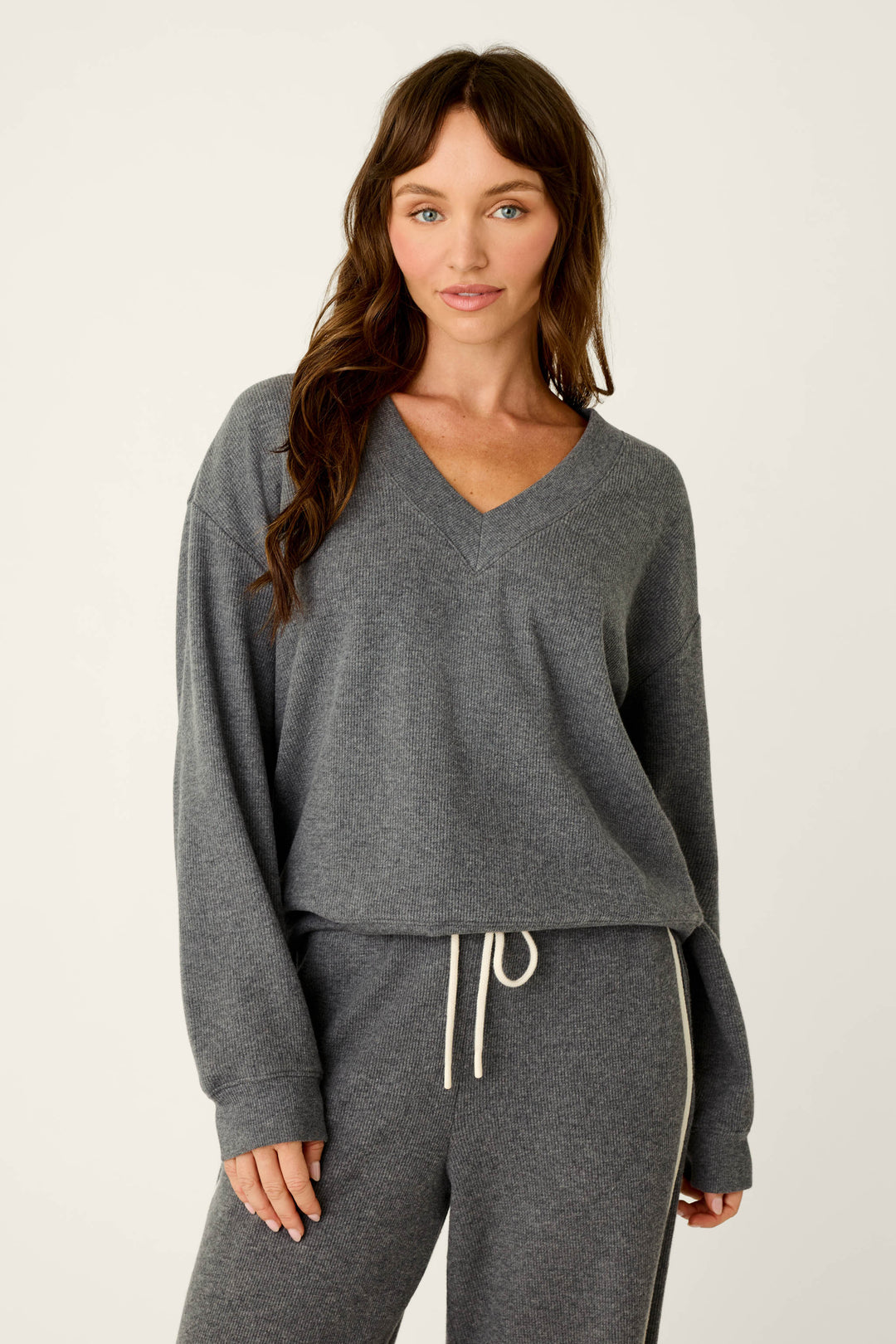A woman wears the P.J. Salvage Weekday Waffles Deep Dive Charcoal Long Sleeve Top, styled with matching charcoal drawstring pants, as she stands against a plain light background.