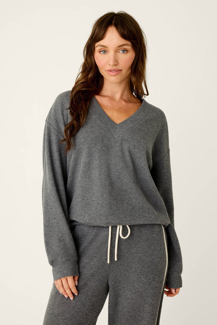 A woman wears the P.J. Salvage Weekday Waffles Deep Dive Charcoal Long Sleeve Top, styled with matching charcoal drawstring pants, as she stands against a plain light background.