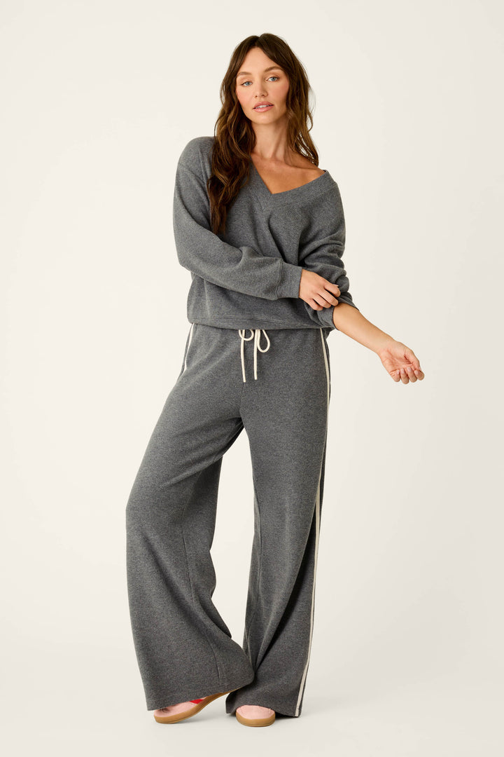 A woman wears the P.J. Salvage Weekday Waffles Deep Dive Charcoal Long Sleeve Top, styled as part of a relaxed lounge set with wide-leg pants featuring white side stripes, standing against a plain background.