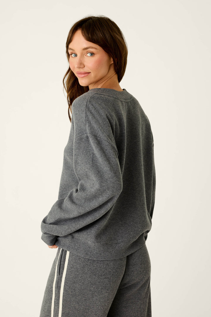 A woman with long brown hair wears the P.J. Salvage Weekday Waffles Deep Dive Charcoal Long Sleeve Top, standing sideways and looking over her shoulder with a slight smile against a plain light background.