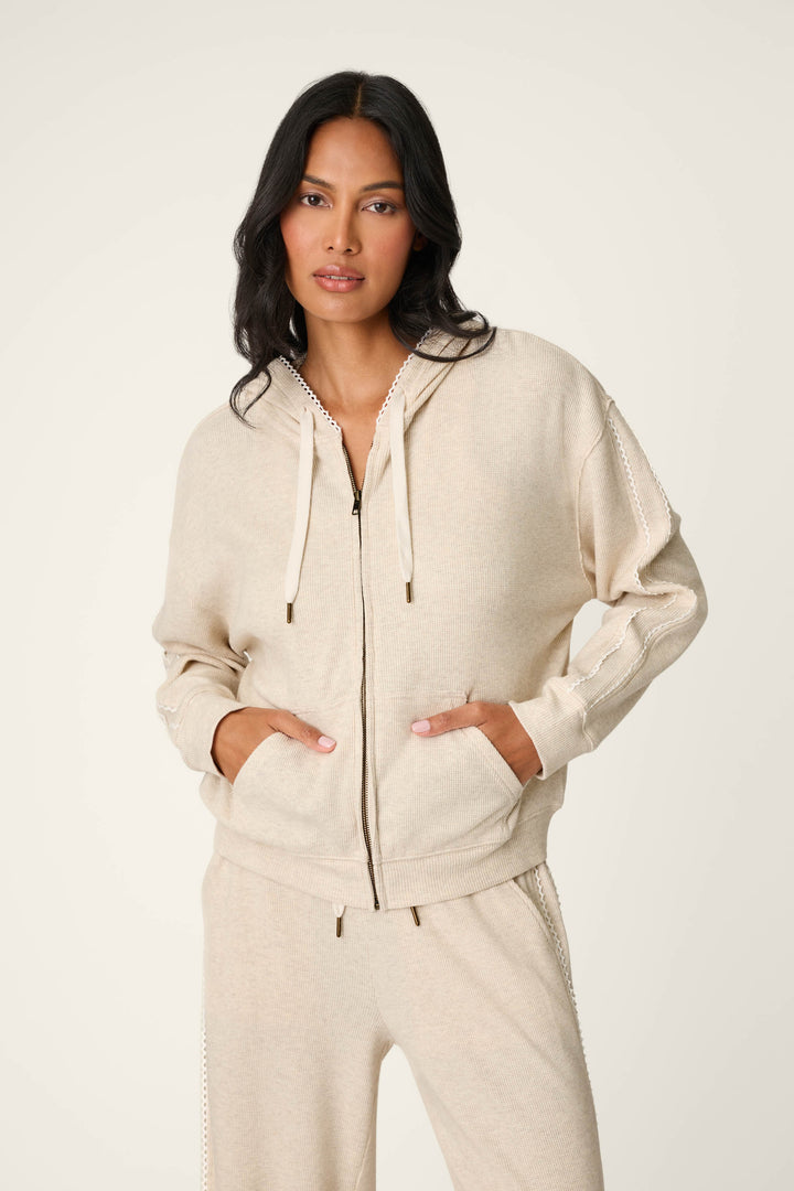 A woman wearing the P.J. Salvage Weekday Waffles Oatmeal Zip-Up Hoodie with front pockets and matching pants stands against a plain light background with her hands in her pockets.