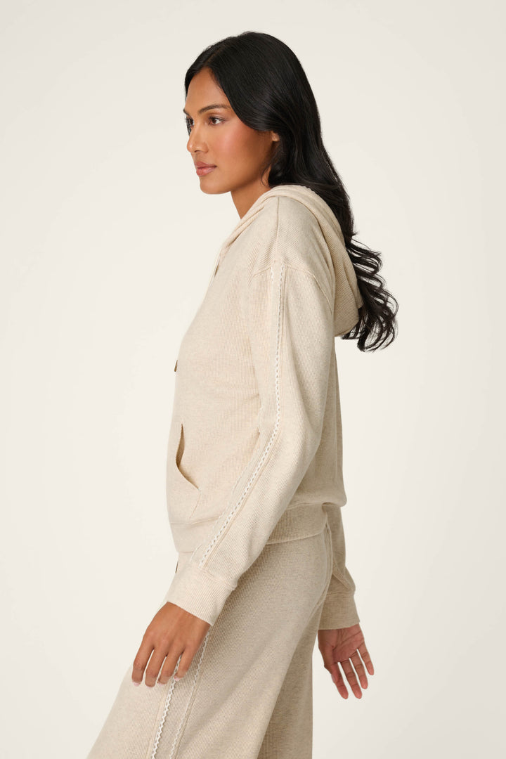 A woman with long dark hair stands in profile against a plain light background, wearing the P.J. Salvage Weekday Waffles Oatmeal Zip-Up Hoodie with matching pants.