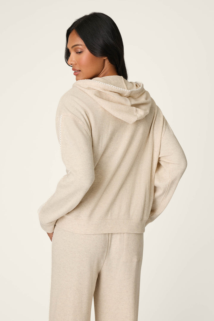 A woman with long dark hair wears the P.J. Salvage Weekday Waffles Oatmeal Zip-Up Hoodie, paired with matching pants, facing away and looking over her shoulder against a plain light background.