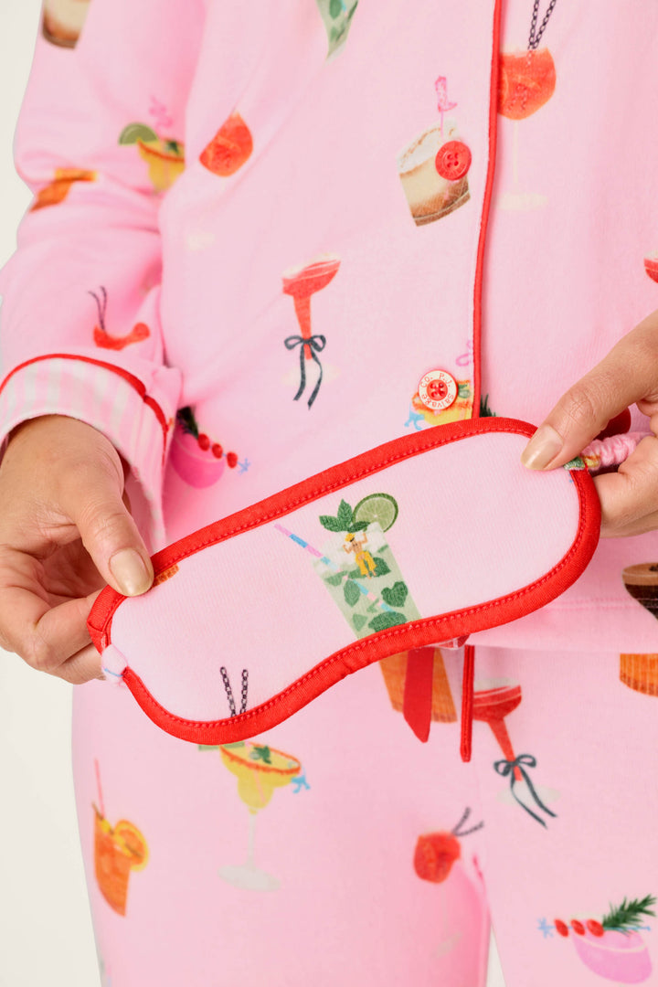 Wearing the P.J. Salvage First Chair, Last Call Cocktail Print 3-Piece PJ Set, a person holds the matching pink and red sleep mask featuring a cocktail design.