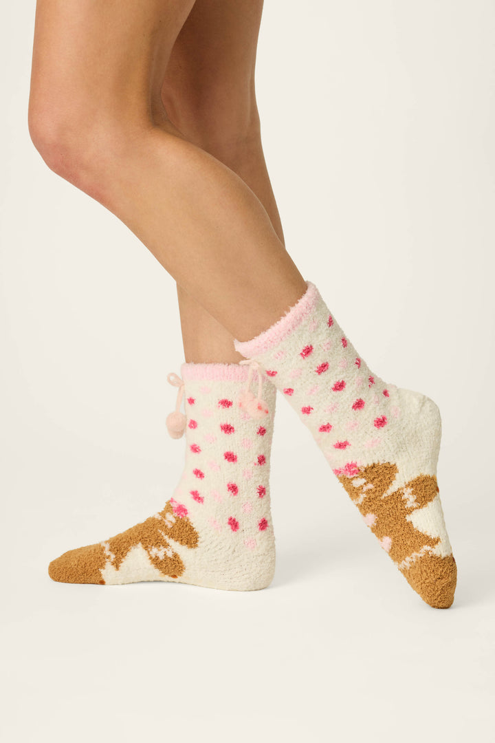 Wearing the Gingerbread Girl & Polka Dots Socks by P.J. Salvage, a person stands on a light background; the cozy cream-colored socks feature pink polka dots and playful brown puppy designs.