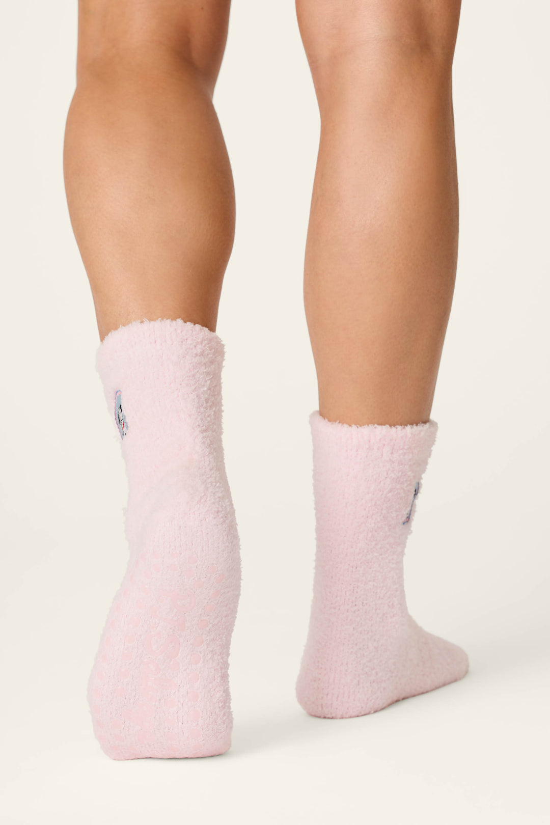 Two legs wearing P.J. Salvage’s Puppy Portrait Socks—soft, fuzzy light pink socks with a cozy texture—are pictured from the back on a plain light background. The socks reach just above the ankles.