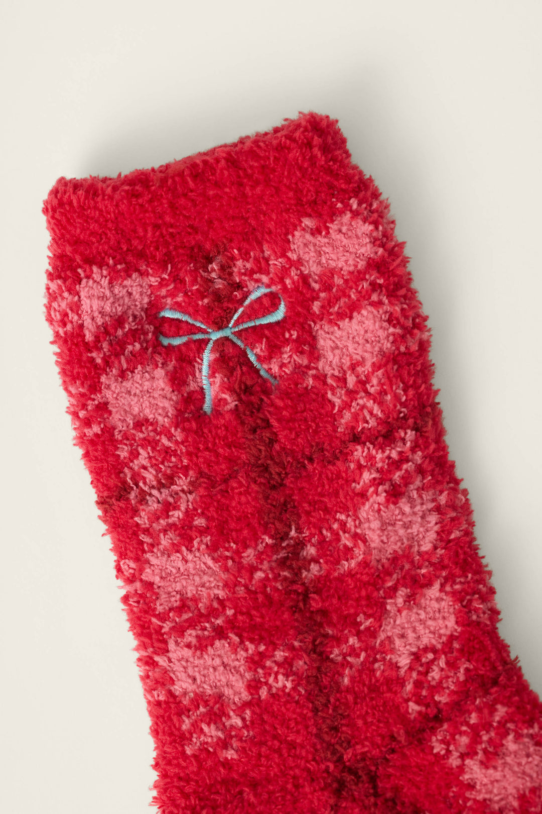 A close-up of the Red Plaid with Embroidered Bow Socks by P.J. Salvage, featuring fluffy red and pink checkered fabric and a small blue embroidered bow near the top cuff, set against an off-white background.