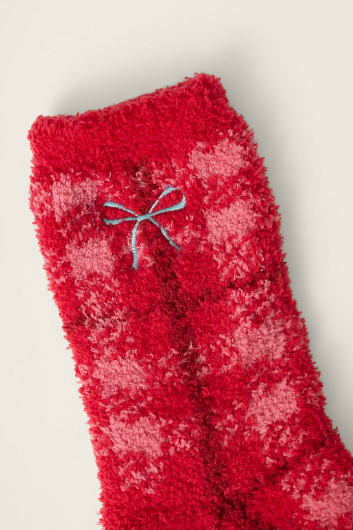 A close-up of the Red Plaid with Embroidered Bow Socks by P.J. Salvage, featuring fluffy red and pink checkered fabric and a small blue embroidered bow near the top cuff, set against an off-white background.