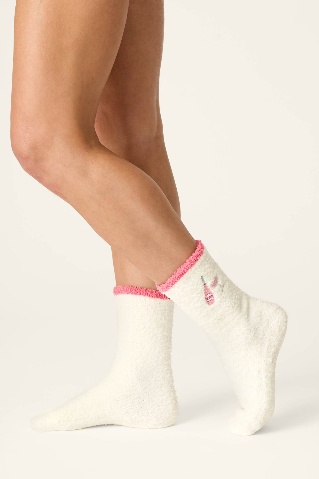 Modeling the Sip, Sip, Sparkle Embroidered Socks by P.J. Salvage, a person stands against a plain light background; the fuzzy white socks feature pink trim and an embroidered bunny face detail on the side.