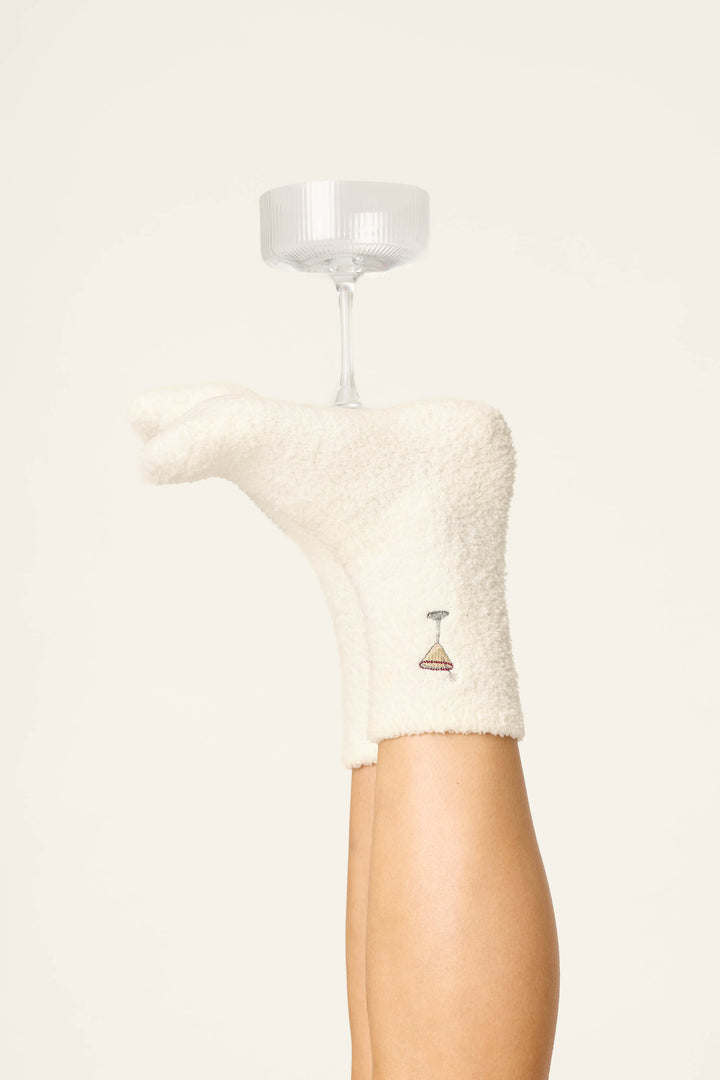 A person's leg raised vertically, wearing P.J. Salvage Holiday Martini Embroidered Socks, with a coupe glass balanced upside down on their foot.