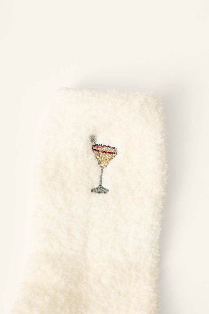 Holiday Martini Embroidered Socks by P.J. Salvage feature a fuzzy white fabric adorned near the center with an embroidered cocktail glass filled with a yellow drink and accented by a pink rim.