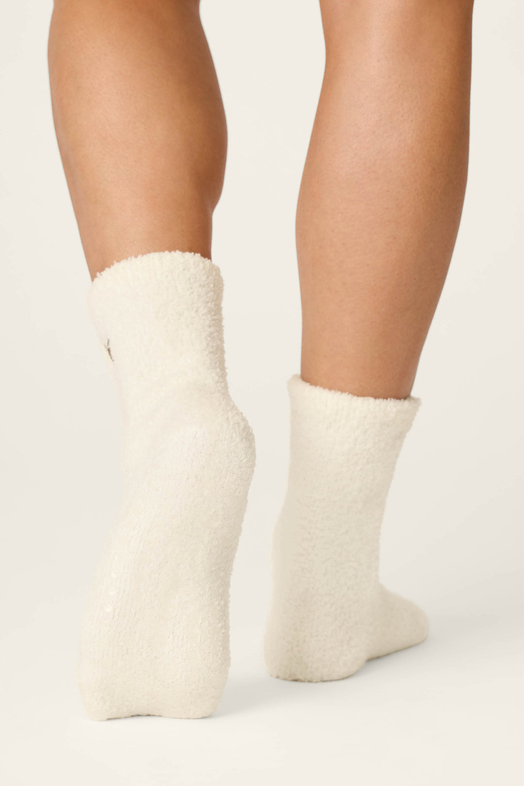 Close-up of the back of a person's lower legs wearing P.J. Salvage Holiday Martini Embroidered Socks, standing on a plain light background.