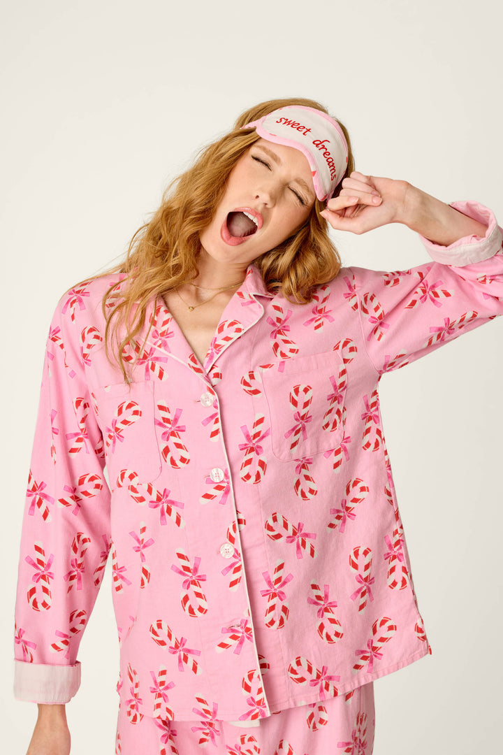 Wearing the P.J. Salvage Sweeter Than Sugar Candy Cane Print 4-Piece PJ Set, a woman yawns and lifts a sweet dreams sleep mask onto her forehead.