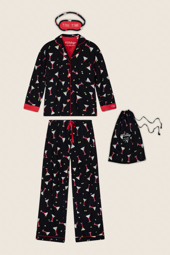 The Christmas Cocktails Martini Print 4-Piece PJ Set by P.J. Salvage features a black pajama set adorned with colorful martini glass prints, red trim, a collared button-down top, and a matching pair of pants with a red drawstring waist tie. The set also includes a coordinating sleep mask labeled “TINI TIME” and a black drawstring bag.