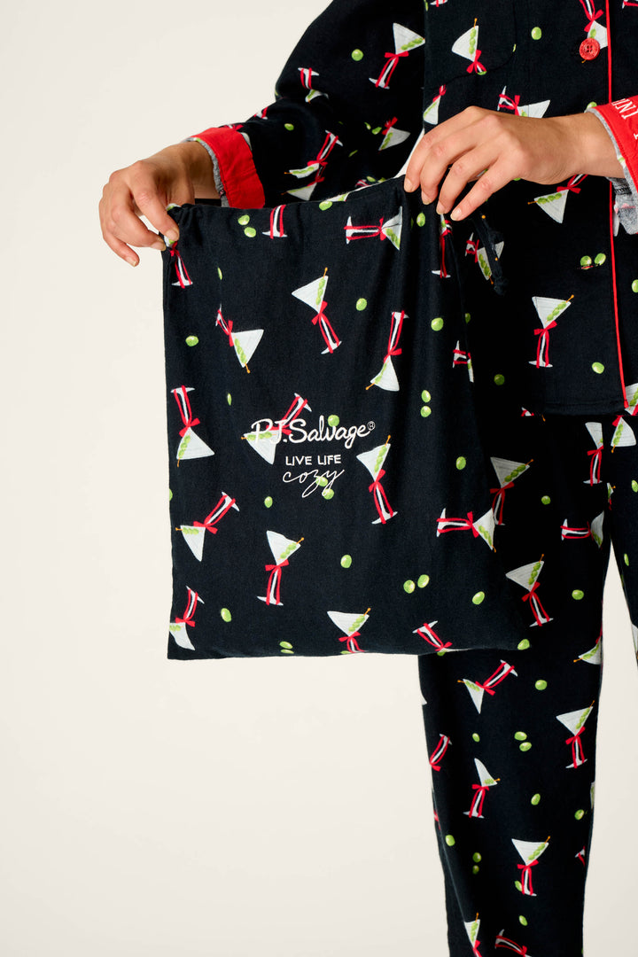 A person wearing the P.J. Salvage Christmas Cocktails Martini Print 4-Piece PJ Set holds a matching drawstring bag that says “PJ Salvage LIVE LIFE Cozy.”.