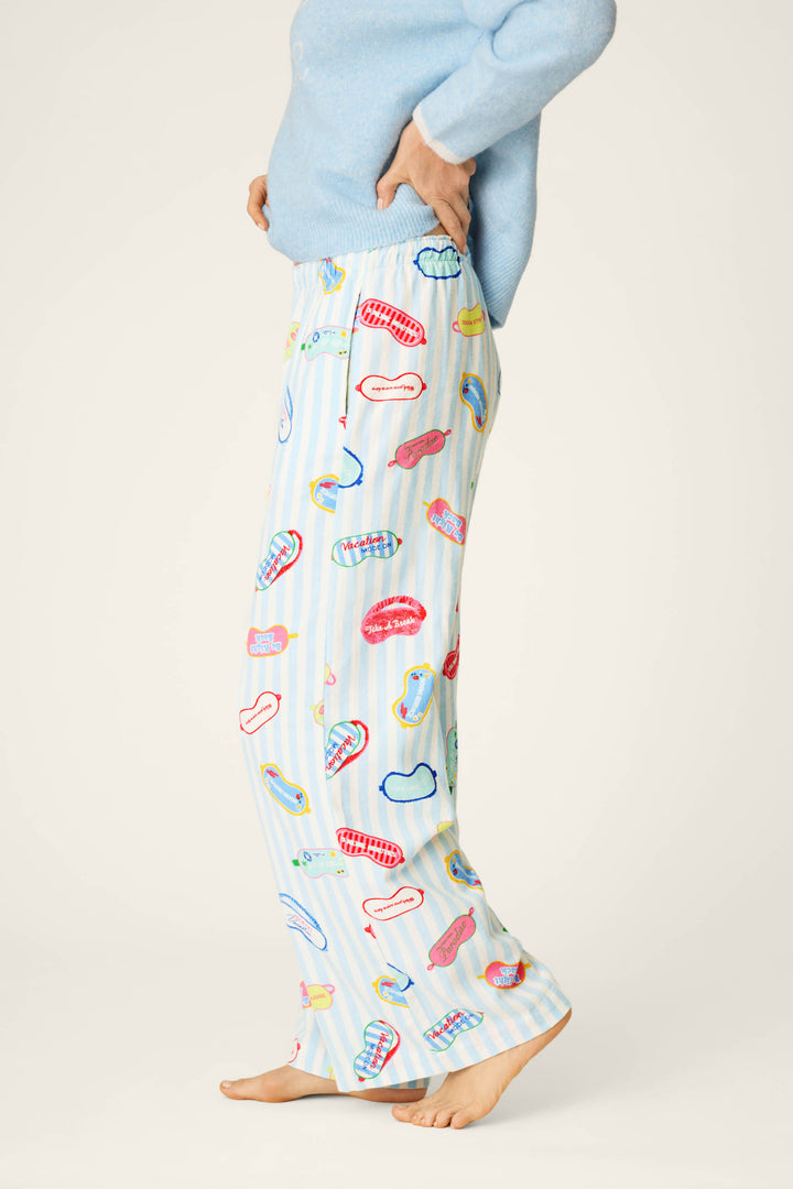 A person is shown from the shoulders down in a side view, standing barefoot on a light background, wearing a light blue sweater and P.J. Salvage Out of Office Eyemask Print Flannel Pajama Pants.