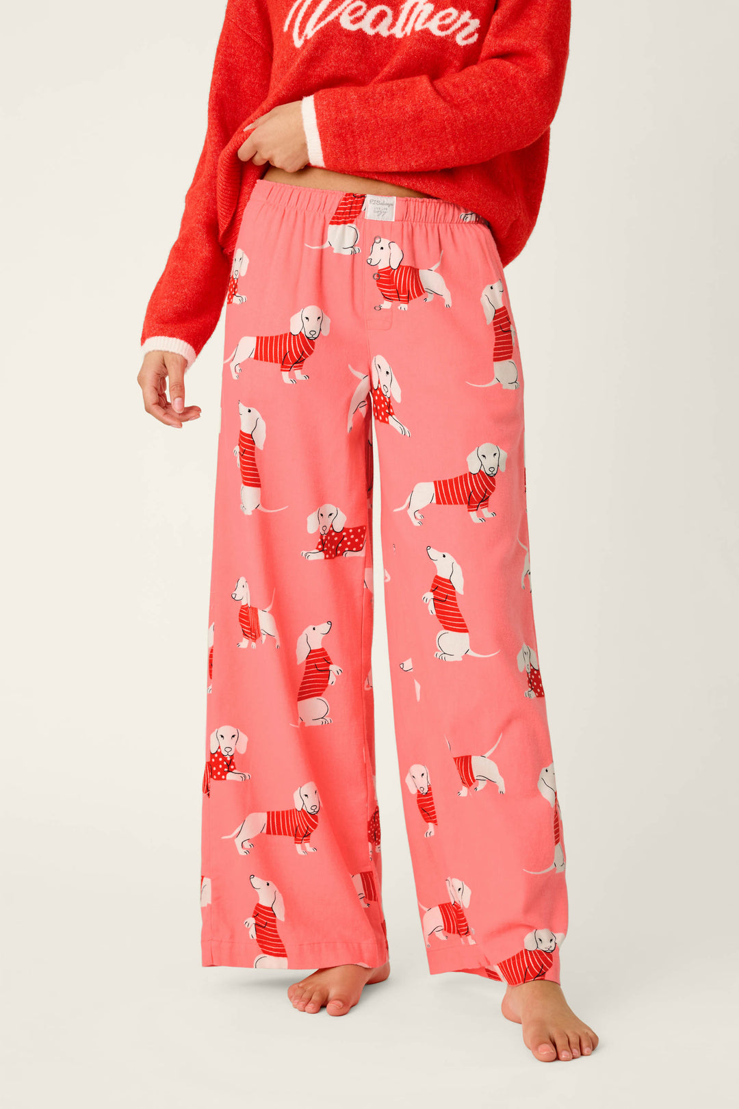 A person wearing P.J. Salvage Dachshund Print Flannel Pajama Pants and a red sweater stands barefoot against a plain background.