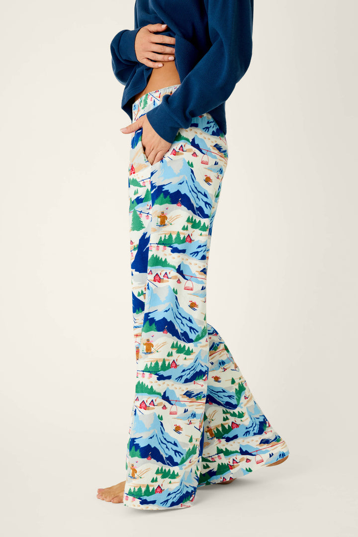 A person wearing P.J. Salvage Ski Ya Later Skiing Bears Print Flannel Pajama Pants, paired with a blue top and standing barefoot against a plain background.