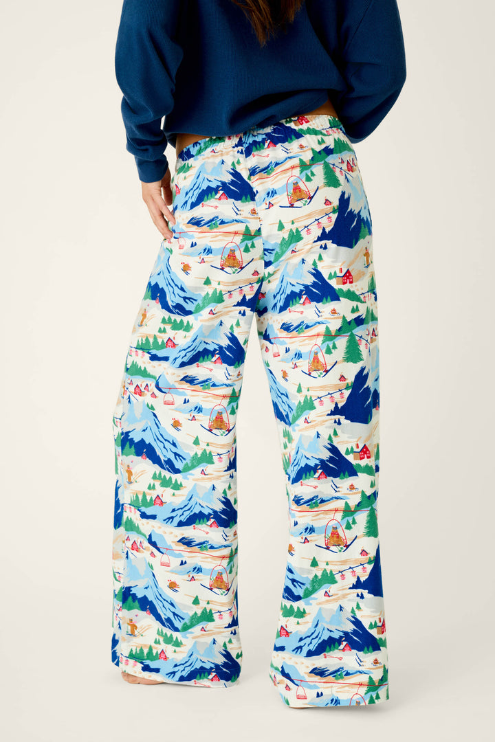 A person wearing P.J. Salvage’s Ski Ya Later Skiing Bears Print Flannel Pajama Pants, featuring a playful mountain, tent, and lake design, stands with their back to the camera against a plain background.