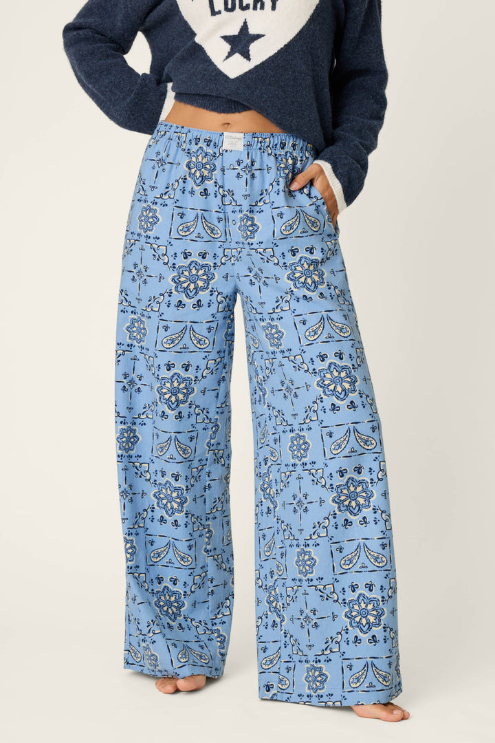 A person is wearing P.J. Salvage Classic Paisley Bandana Print Flannel Pajama Pants, featuring a wide-leg silhouette and a light blue paisley bandana pattern. Only the lower half of the body is visible.