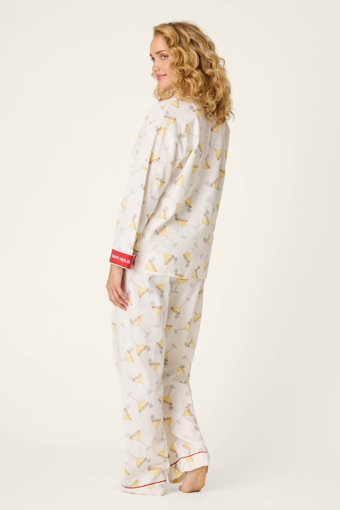 A person with curly blonde hair, wearing the P.J. Salvage Happy Hour Cocktail Print 3-Piece Flannel PJ Set, stands barefoot and slightly turned to the side, smiling over their shoulder against a plain light background.