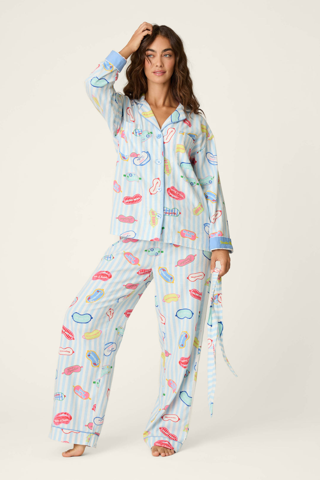 A woman poses in the P.J. Salvage Out of Office Eyemask Print 3-Piece Flannel PJ Set, featuring a playful pattern of lips, bananas, and other colorful designs on a light blue background with vertical stripes.