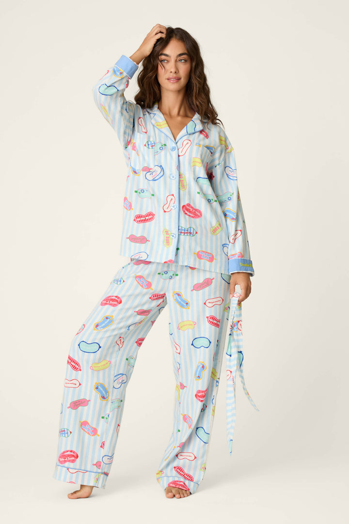 A woman poses in the P.J. Salvage Out of Office Eyemask Print 3-Piece Flannel PJ Set, featuring a playful pattern of lips, bananas, and other colorful designs on a light blue background with vertical stripes.